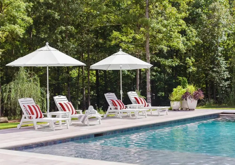 Resort-inspired pool deck featuring white Nautical chaise lounges with striped cushions and large umbrellas beside a swimming pool.